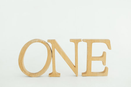 Letters carved from wood, the word one, stand on a white backgroundの写真素材