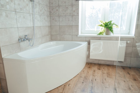 Corner acrylic bathtub with plastic front screen underneath in a bathroom with a window.