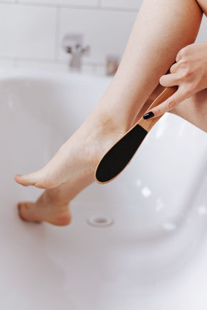 The young woman cleaning her feet, uses heel scrubber in bathroom