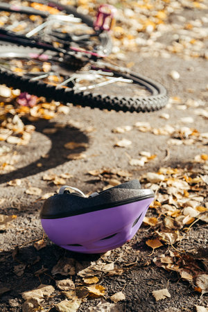 Purple helmet lies abandoned on the pavement beside a toppled bicycle, surrounded by scattered autumn leaves evidence of a sudden fallの写真素材