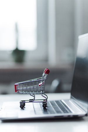 A tiny shopping cart sits on the keyboard of a laptop, symbolizing online shopping, e-commerce