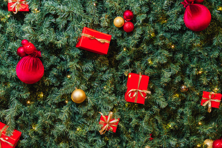 Christmas tree branches background adorned with red ornaments, golden baubles, and gift boxes. New...