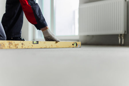Hands Holding Worn Spirit Level On Concrete Floor. Manual Alignment Tool In Construction Workflow