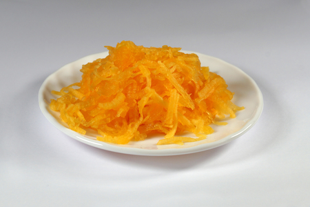 Pumpkin is grated with grater on a chopping board lined with a white plateの写真素材
