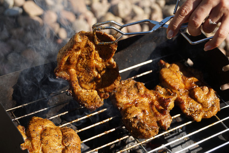 Grilled meat, barbecue, tongs, charcoal smoke. Female hand transferring meat to the other sideの写真素材