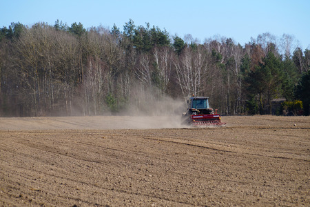 A tractor in the clouds of dust created when harrowing dry soil. Spring field work.の写真素材