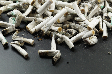 Heap of white cigarette butts, slim type and scattered ash. Dark backgroundの写真素材