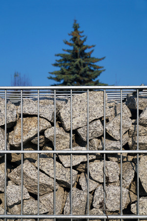 Close-up on a gabion filled with granite splinters. Sky and pine in the background.の素材 [FY310123026267]