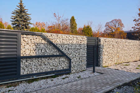 Automatic entrance gate and wicket integrated into the wall made of a gabion. A fence made of gabions.の写真素材