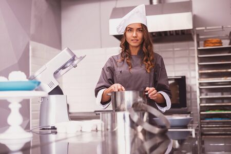 Beautiful young woman in chef hat is holding wooden spoon, looking at camera and smilingの写真素材