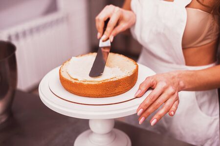 Beautiful housewife in apron smears cream cakeの写真素材