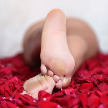 Pair of well-groomed feet against from petals of red rosesの写真素材