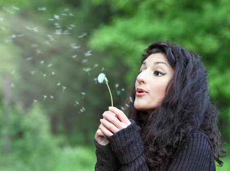 Summer fun, young beautiful woman with magnificent hair, blowing dandelion on the meadowの写真素材