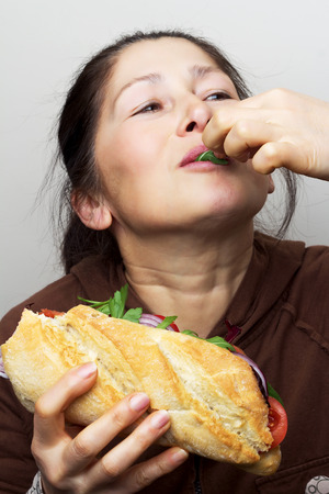 Woman with a sandwich with tomatoes, bell pepper,red onion and arugula.の写真素材