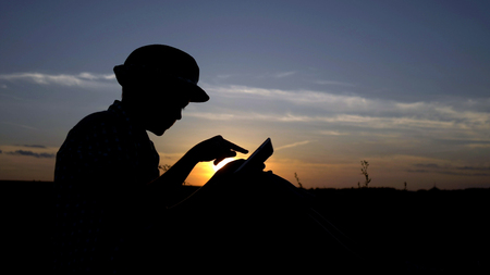 silhouette of a boy uses a tablet at sunset in the field, reads something on the tablet, outdoorsの写真素材