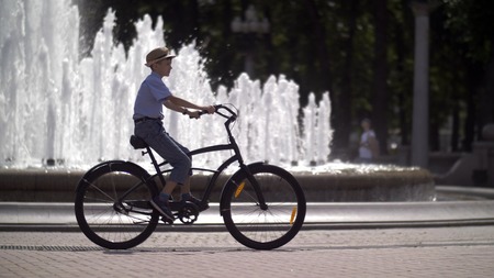 happy boy in a hat rides a bike in the city park against the background of a fountainの写真素材
