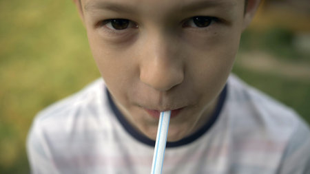 happy boy drinks a drink through a straw and looks into the cameraの写真素材