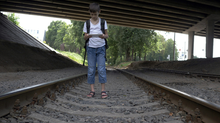 traveler boy is walking along the railroad tracks looks at the tabletの写真素材