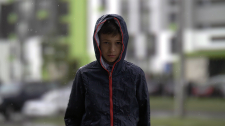 portrait Offended sad boy is standing in the rain and looks into the cameraの写真素材