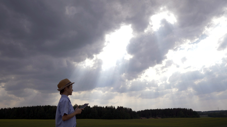boy uses a tablet on a background of beautiful clouds, looks at the skyの写真素材