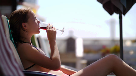girl is drinking juice lying on a lounger near a swimming pool