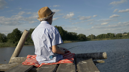 boy sits on the pier and catches fishの写真素材