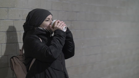 pretty woman warming in winter in a tunnel and enjoying coffee