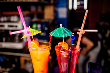 Fresh tall glass of tropical cocktail with juice at bar counter background. Cocktail glasses with ice and holiday lights in the background. Margarita cocktail in a glass on a background of bright lightsの写真素材