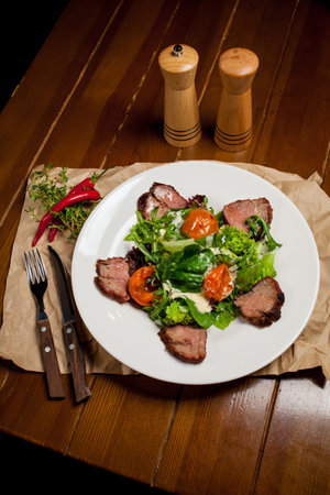 Meat beef steaks with greens, apricots and sauce on a large white plate on food mat - bamboo mat for food background. There are cutlery, a wooden pepper shaker and a salt shaker. barbeque, BBQの写真素材