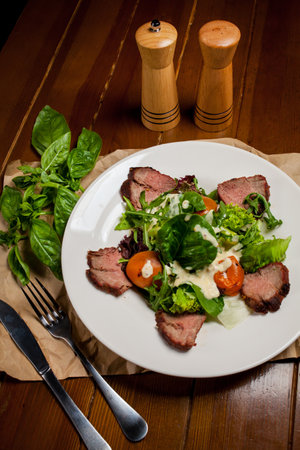 Meat beef steaks with greens, apricots and sauce on a large white plate on food mat - bamboo mat for food background. There are cutlery, a wooden pepper shaker and a salt shaker. barbeque, BBQの写真素材