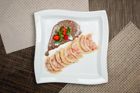 Vareniki with strawberries, mint on a large white plate, on food mat - bamboo mat background Next to the knife and fork - cutlery. Lenten, vegetarian menu - vareniki with cherries and strawberry sauceの写真素材