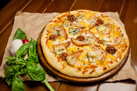 Pizza with pear, walnuts, Dorbl cheese and lemon oil. Homemade pizza with pear, walnuts and gorgonzola on a brown wooden table - craft paper. Next to the pizza is a mushroom, sorrel and cherry tomato.の写真素材