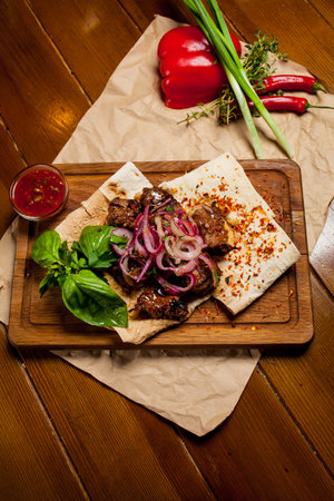 Skewers of lamb with sauce, with onions, lavash. Turkish and Arabic - Oriental traditional kebab with vegetables, onions, tomatoes, bell peppers, pita bread and lettuce on a wooden background.の写真素材