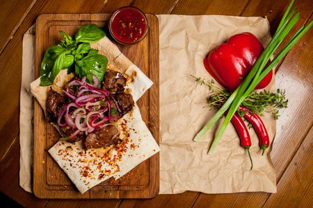Skewers of lamb with sauce, with onions, lavash. Turkish and Arabic - Oriental traditional kebab with vegetables, onions, tomatoes, bell peppers, pita bread and lettuce on a wooden background.の写真素材