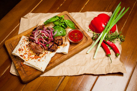 Skewers of lamb with sauce, with onions, lavash. Turkish and Arabic - Oriental traditional kebab with vegetables, onions, tomatoes, bell peppers, pita bread and lettuce on a wooden background.の写真素材
