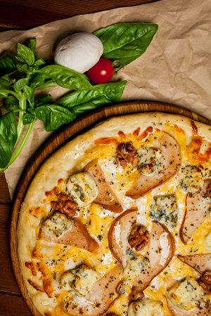 Pizza with pear, walnuts, Dorbl cheese and lemon oil. Homemade pizza with pear, walnuts and gorgonzola on a brown wooden table - craft paper. Next to the pizza is a mushroom, sorrel and cherry tomato.の写真素材