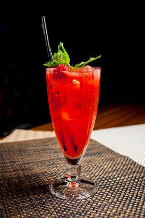 Red strawberry alcoholic cocktail with mint and straw. Alcoholic or non-alcoholic cocktail in a long, tall and narrow clear glass with a dark red liquid and syrup and mint on a dark backgroundの写真素材