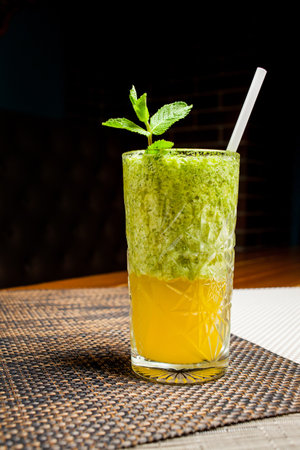 Green cocktail with fruit pulp and straw. Green cocktail with cucumber and parsley as a healthy summer drink on a dark background.の写真素材