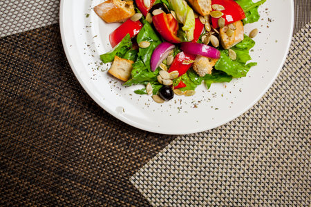 Fresh summer light salad of tomatoes, bread, greens, black olives, sunflower seed, on a large white plate on food mat - bamboo mat for food backgroundの写真素材