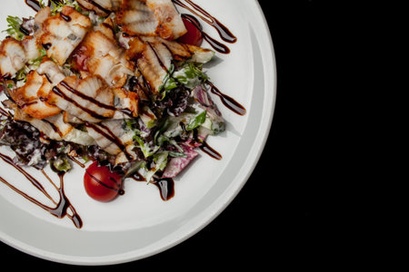 Salad with squid, lettuce, cabbage, cherry tomatoes and sauce. Salad with slices of squid, on a white plate, on a black background. photo close-up, soft focus. Photo for recipe book, restaurant menuの写真素材