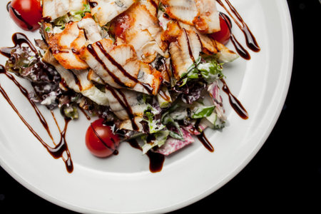 Salad with squid, lettuce, cabbage, cherry tomatoes and sauce. Salad with slices of squid, on a white plate, on a black background. photo close-up, soft focus. Photo for recipe book, restaurant menuの写真素材