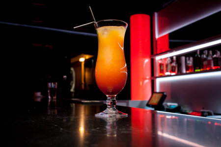 Alcoholic orange cocktail is on the bar. Glass of cocktail on bar background. Fresh cocktail with orange and ice. Alcoholic, non-alcoholic drink-beverage at the bar counter in the night club.の写真素材