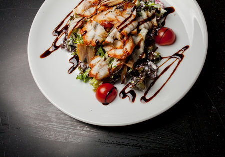 Salad with squid, lettuce, cabbage, cherry tomatoes and sauce. Salad with slices of squid, on a white plate, on a black background. photo close-up, soft focus. Photo for recipe book, restaurant menuの写真素材