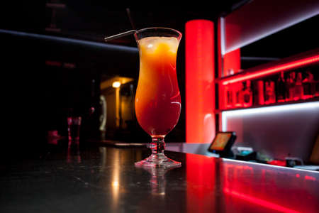 Alcoholic orange cocktail is on the bar. Glass of cocktail on bar background. Fresh cocktail with orange and ice. Alcoholic, non-alcoholic drink-beverage at the bar counter in the night club.の写真素材