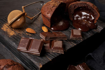 homemade muffins with chocolate, chocolate bars and almonds grains on a black wooden background. Cook prepares muffins with chocolate in the kitchen. Cook prepares muffins with chocolate in the bar.の写真素材