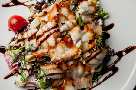 Salad with squid, lettuce, cabbage, cherry tomatoes and sauce. Salad with slices of squid, on a white plate, on a black background. photo close-up, soft focus. Photo for recipe book, restaurant menuの写真素材