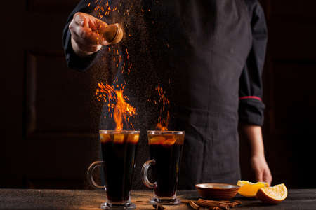 Preparation of mulled wine to serve, in a restaurant. Mulled wine in the preparation of the chef's bar. The hands of the chef on a dark black background. Burning mulled wine with sparks.の写真素材