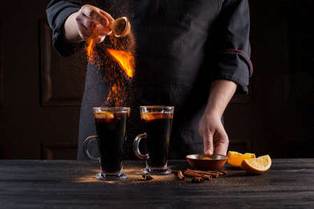 Preparation of mulled wine to serve, in a restaurant. Mulled wine in the preparation of the chef's bar. The hands of the chef on a dark black background. Burning mulled wine with sparks.の写真素材