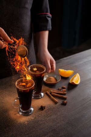 Preparation of mulled wine to serve, in a restaurant. Mulled wine in the preparation of the chef's bar. The hands of the chef on a dark black background. Burning mulled wine with sparks.の写真素材