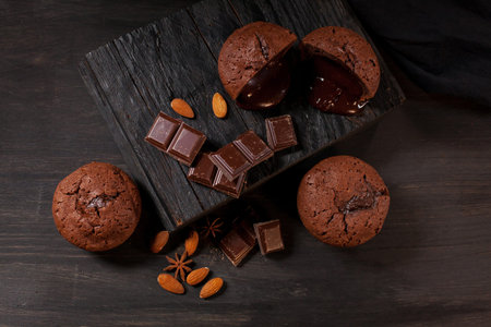 homemade muffins with chocolate, chocolate bars and almonds grains on a black wooden background....